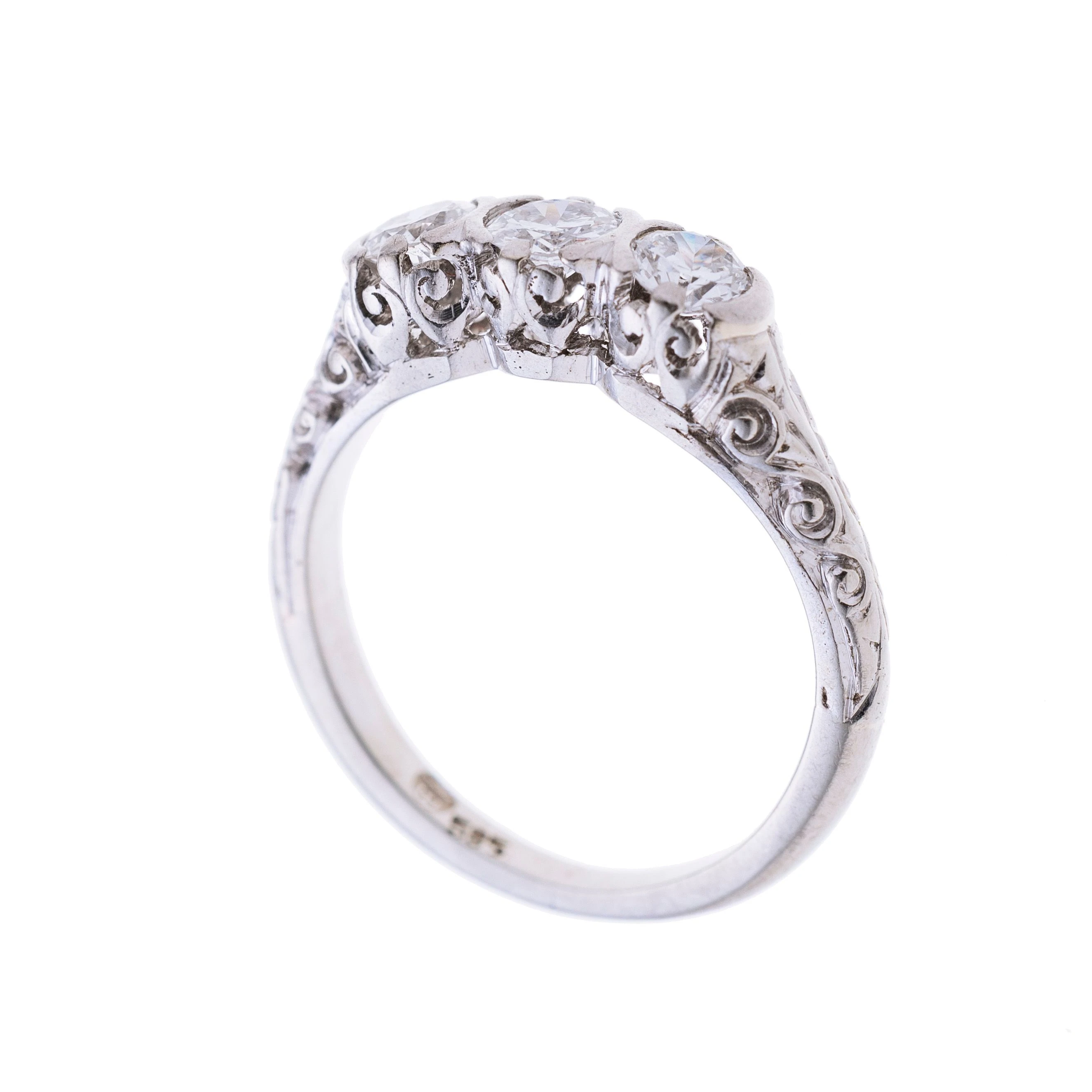 Ein Trilogie-Ring besetzt mit drei Diamanten. Die Ringschultern sind floral verziert.