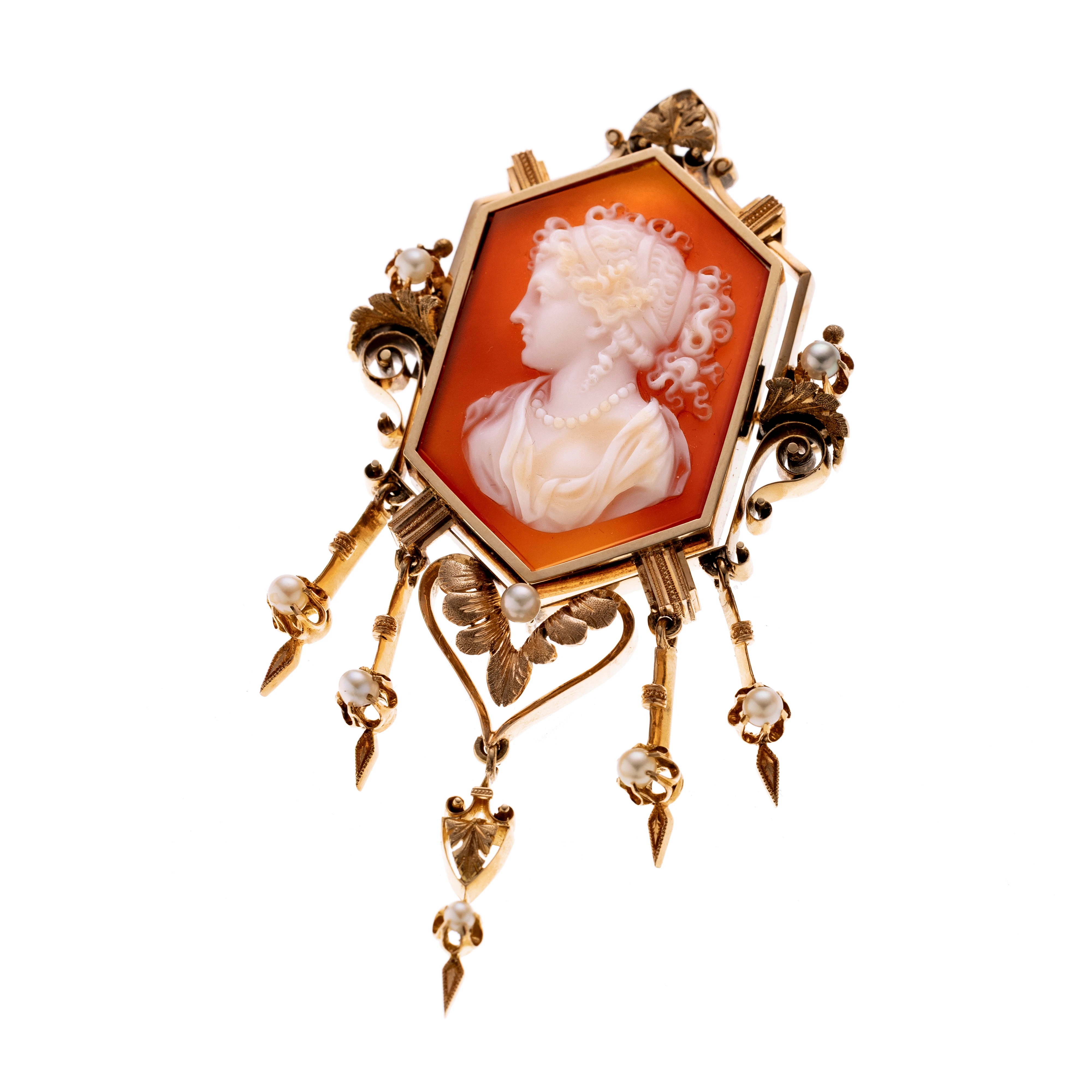 Anhängerbrosche im historischen Stil. Im Zentrum eine fein geschnittene Kamee, die das nach links blickende Profil einer Dame mit kunstvoll gelockter Frisur und Perlenschmuck zeigt. Die sechseckige Fassung ist reich ornamental gestaltet und wird von filigranen Voluten, Blütenmotiven und Saatperlen akzentuiert. Lebendigkeit verleihen 5 Pendeloque-Elemente, die ebenfalls Perlbesetz und Verzierungen tragen