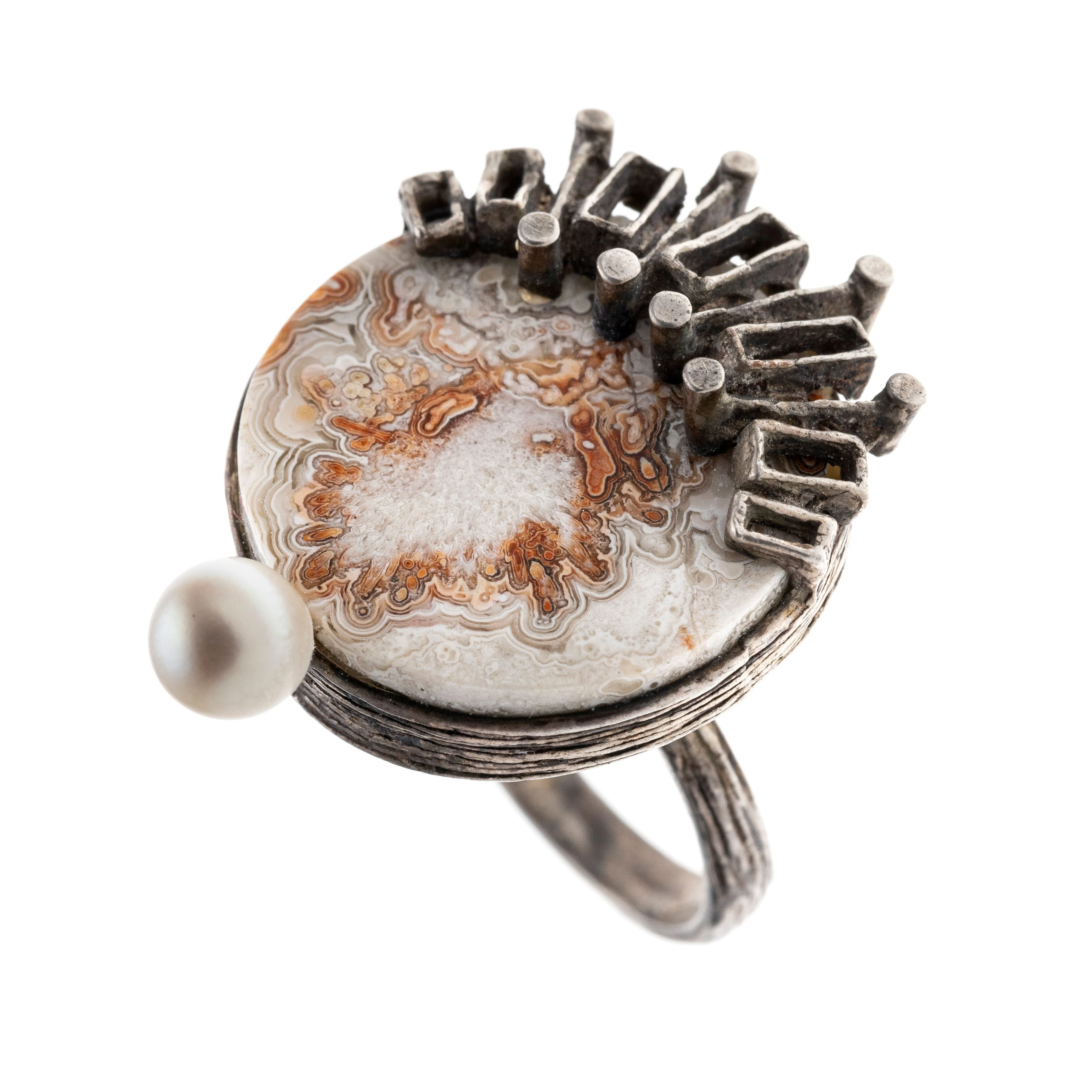 Ein Ring mit einer runden Achatscheibe, einer zierenden Perle und abstrakter Ornamentik als Ringkopf. Autorenschmuck.
