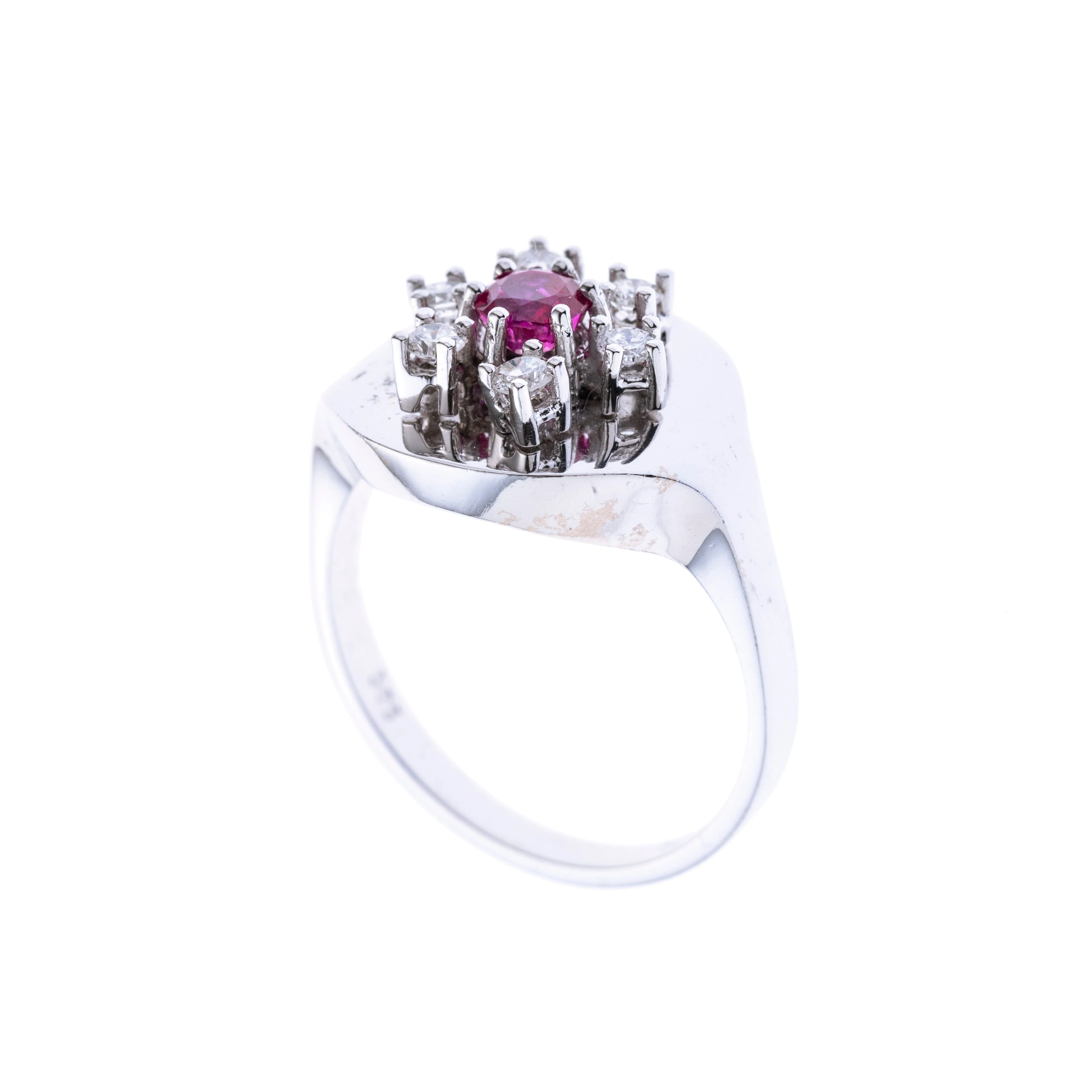 Ein runder Ringkopf mit einem erhöht gefassten ca. 0.20 ct. Rubin, der von sechs Brillanten gerahmt wird.