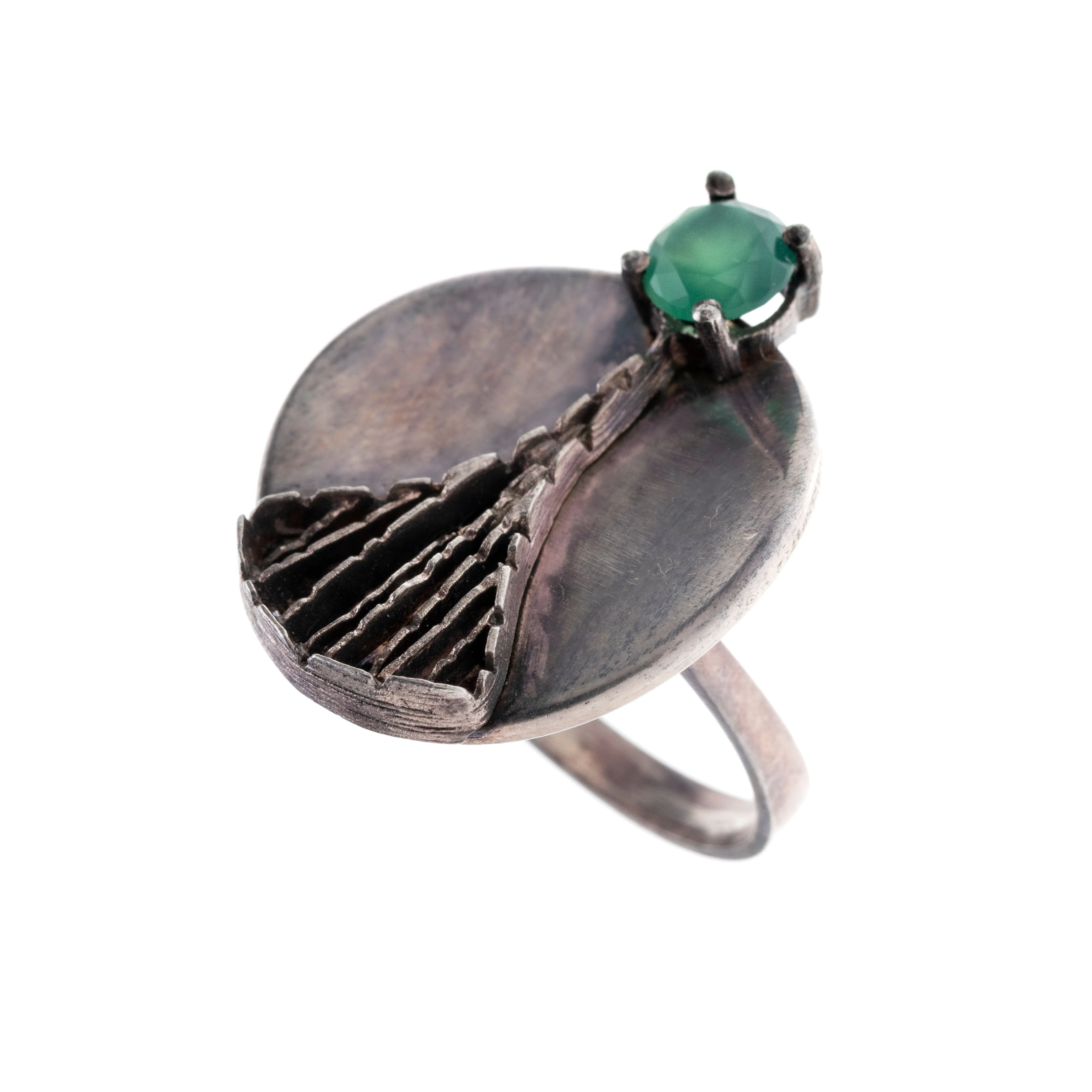 Ein Ring mit rundem Ringkopf, abstrakt zulaufendem Geflecht und einem grünen Glasstein. Autorenschmuck.