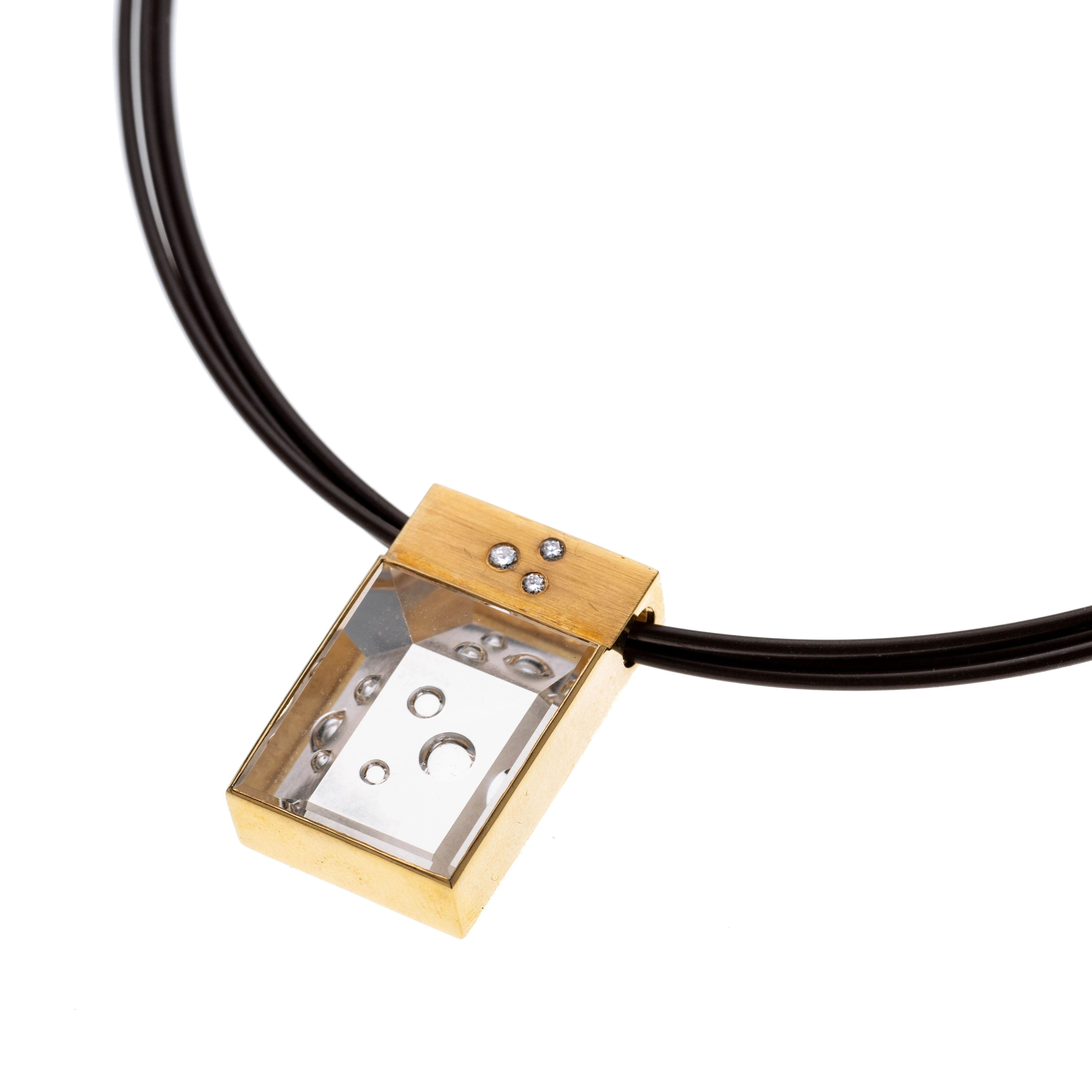 Ein Rechteckiger Bergkristall mit Blubb 35,08 ct. unter einem rechteckigem Geldgoldelement mit drei eingeriebenen Diamanten gefasst und an einem braunen dreisträngigen Edelstahl-Silikon-Reif.