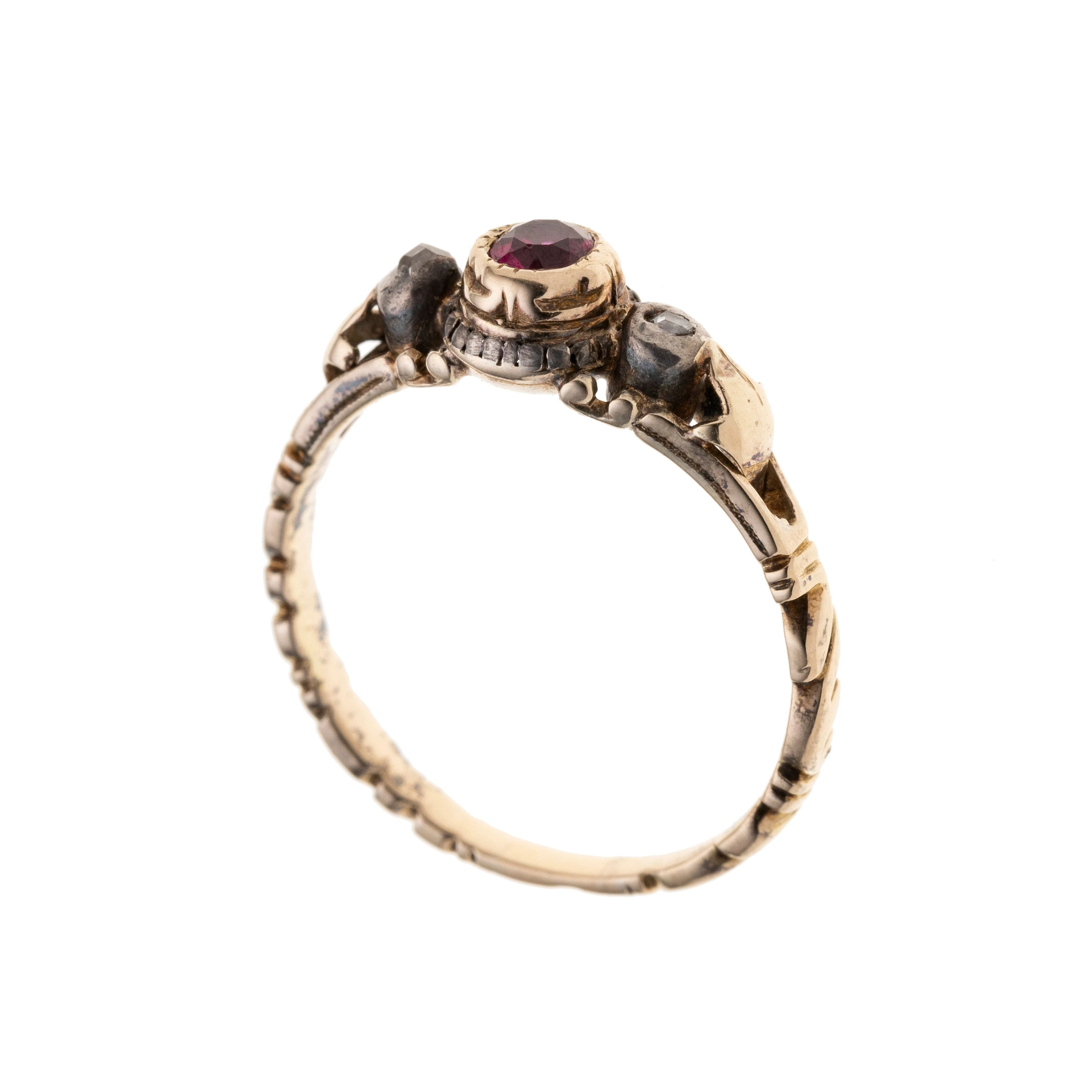 Ein zarter, verschnörkelter Ring, mittig mit einem Rubin, der seitlich von je einer Diamantrose gerahmt wird.