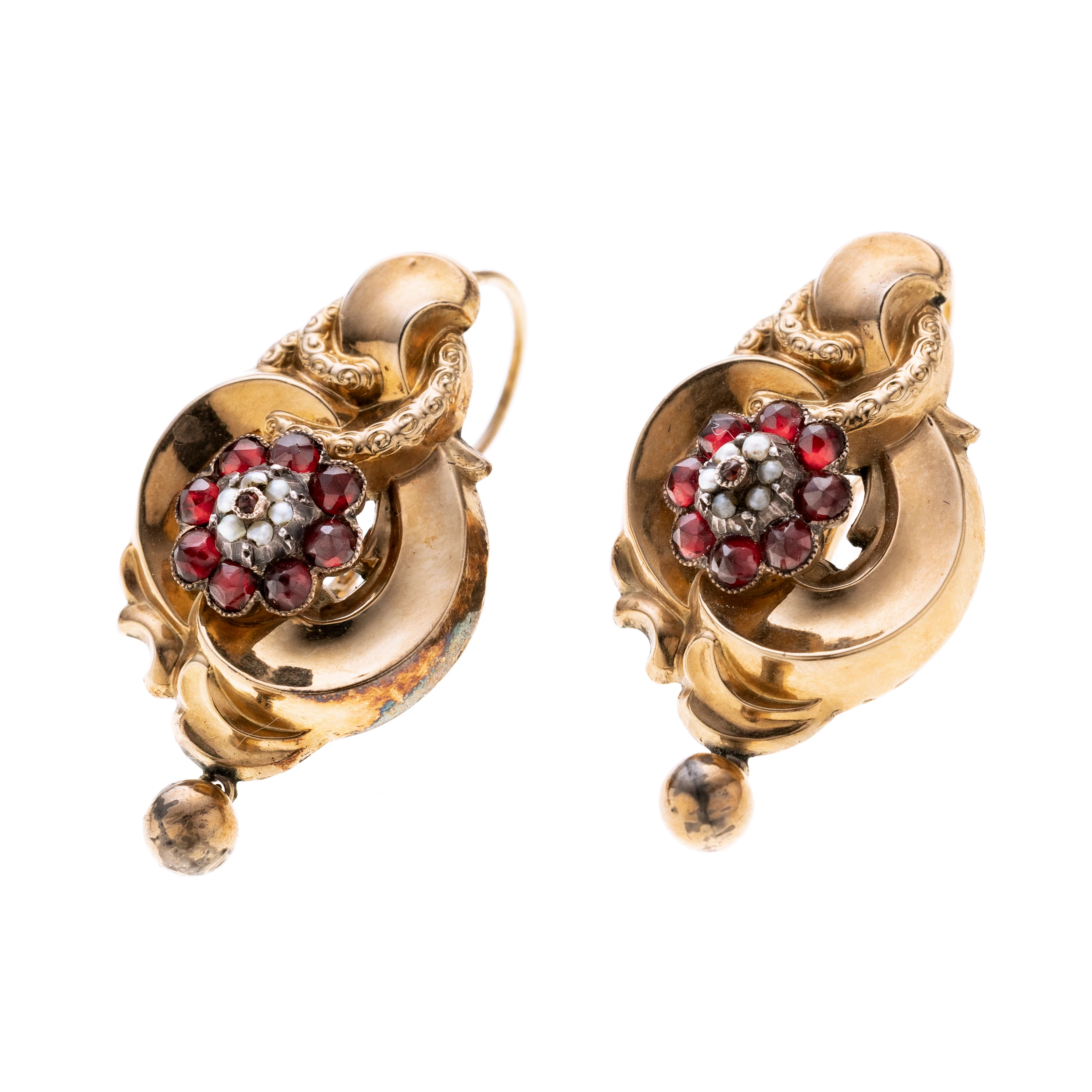 Ein Paar Ohrhänger im historischen Stil. Jede der Kompositionen zeigt eine fein ausgearbeitete ornamental geschwungene, barocke Rahmung, in deren Zentrum ein Bouquet aus tief rubinrot funkelnden Granaten gefasst ist, die wiederum eine Rosette aus 6 Saarperlchen rahmen. Am unteren Abschluß jedes Ohrhängers schwingt eine kleine Goldkugel.
