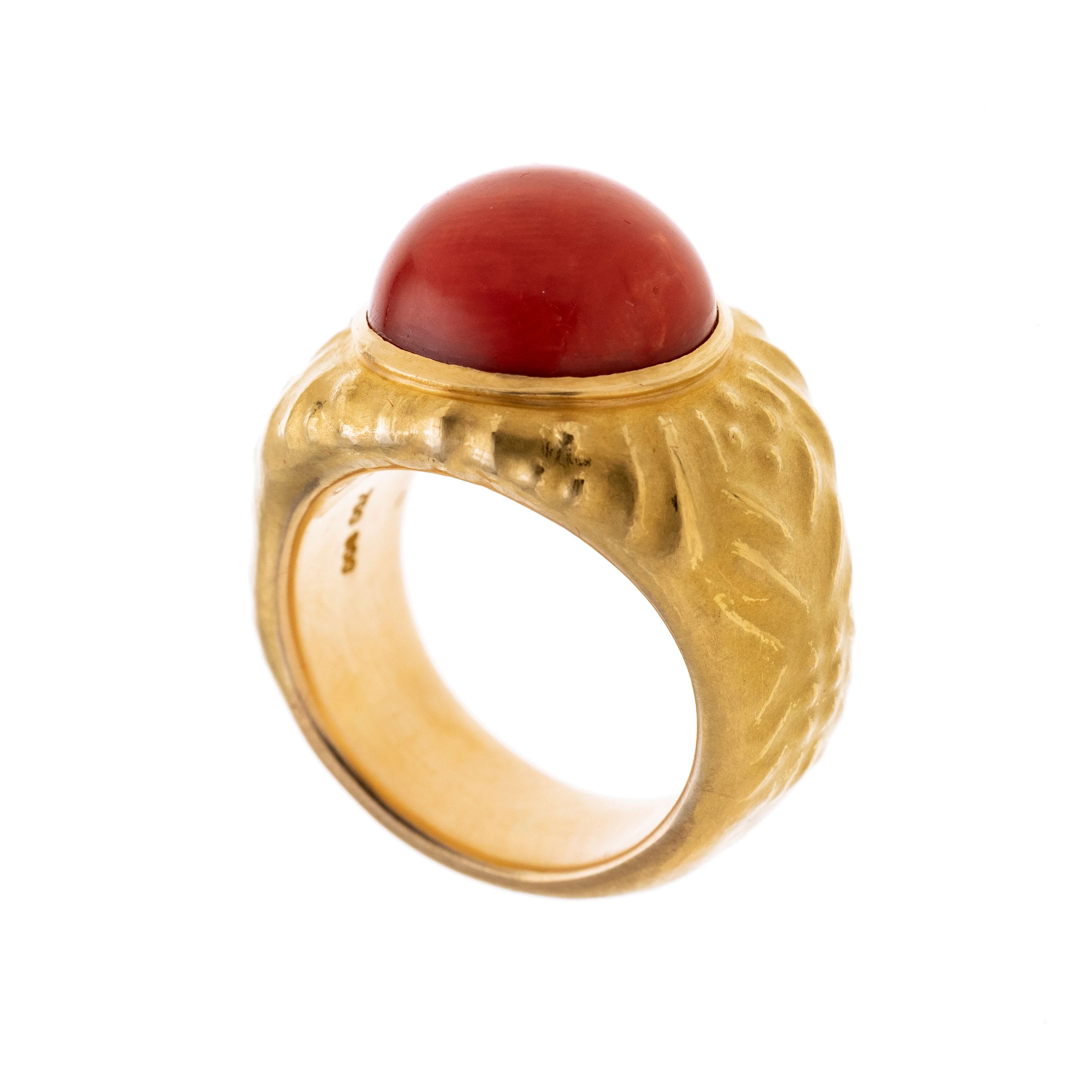 Ein runder Korallen-Cabochon in Zarge, flankiert von ornamentierten, ziselierten Ringschultern.